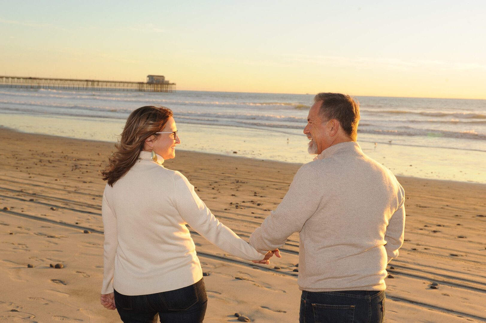 A man and woman holding hands on the beach.