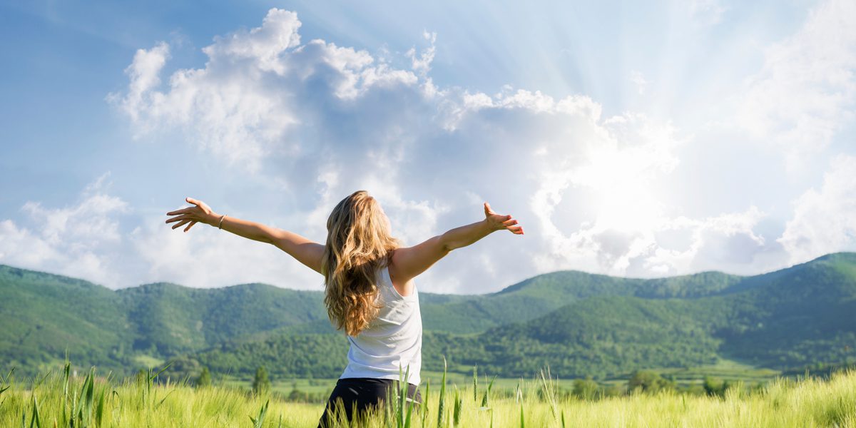 A woman standing in the grass with her arms outstretched.