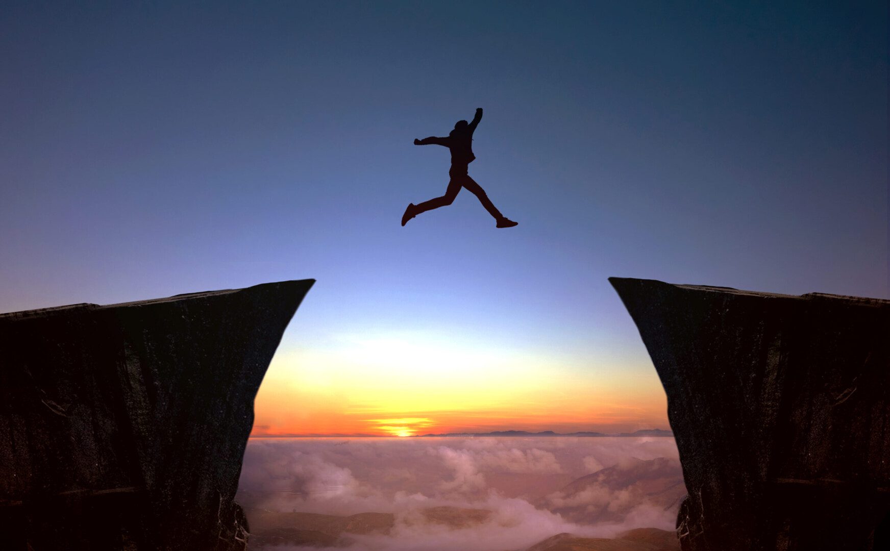 A man jumping over two cliffs at sunset.