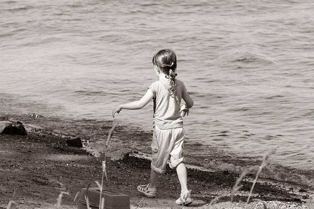A little girl walking along the shore of a lake.