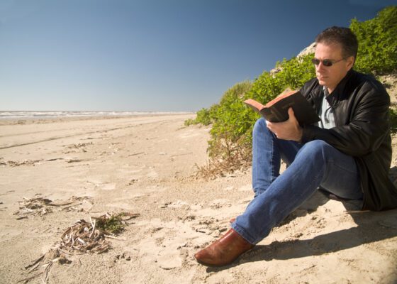 A man sitting on the beach reading a book.