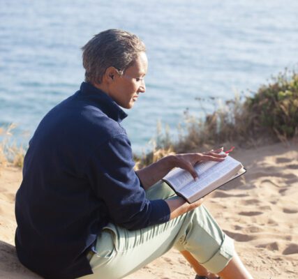 A man sitting on the beach writing in his notebook.