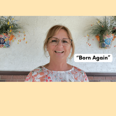 A woman with glasses and a floral shirt is smiling.